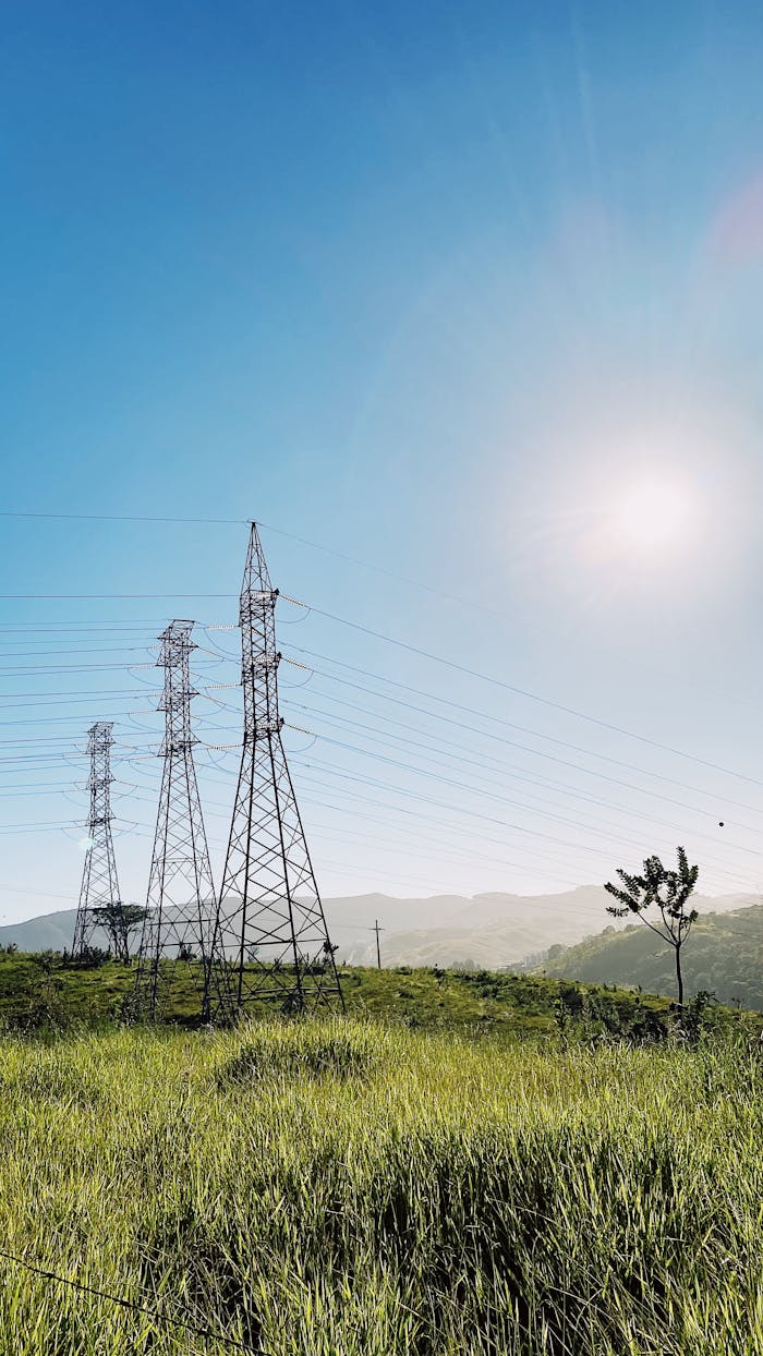 Electric pylons and power lines in a lush green field under a bright sunny sky.