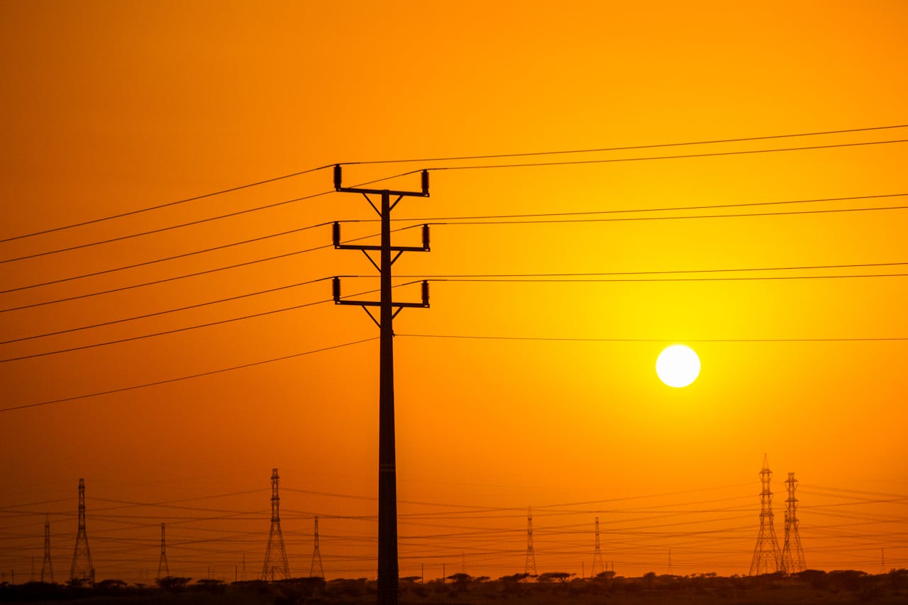 Silhouette of power lines and pylons against a vibrant orange sky at sunset.