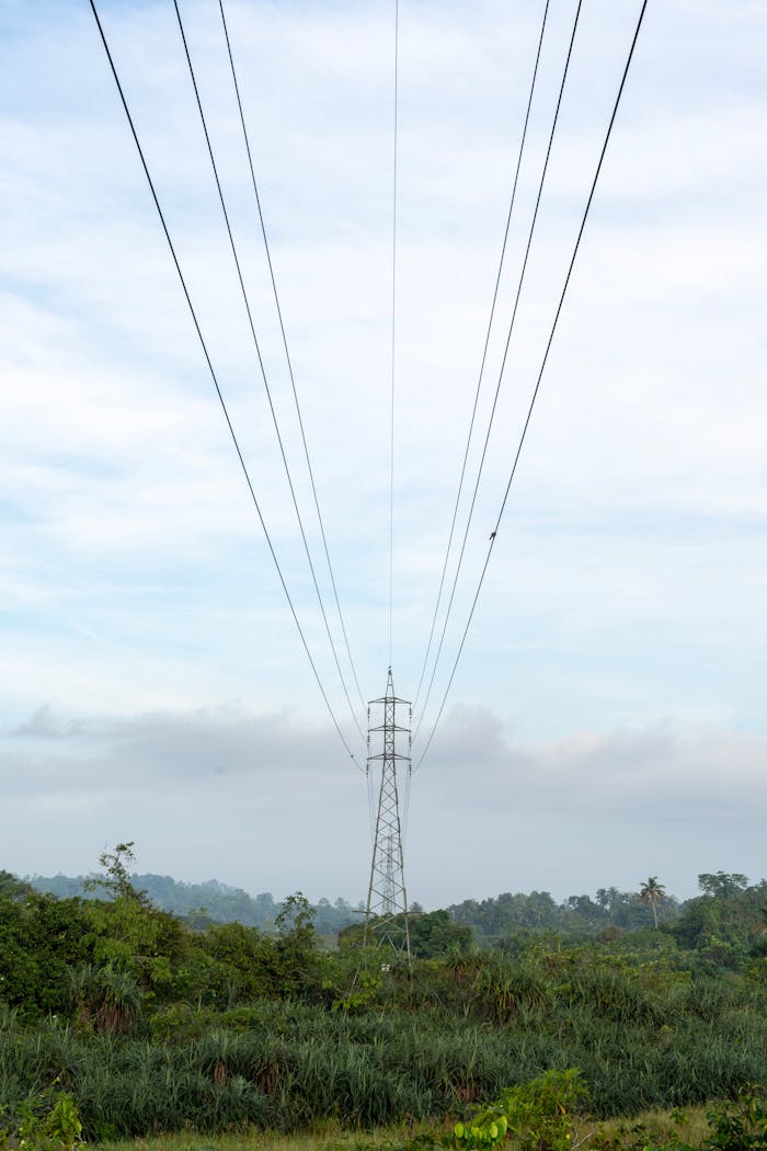 About A tall electricity pylon with power lines in a green field against a cloudy sky.